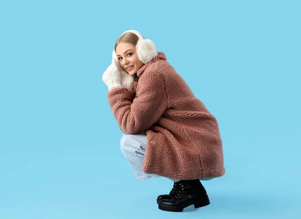 Beautiful Smiling Woman Winter Clothes Fur Earmuffs Squatting Blue Background — Stock Photo, Image