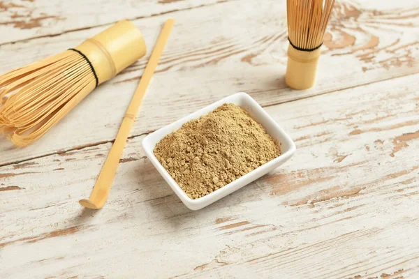 Beyaz ahşap arka planda hojicha tozu, chasen ve chashaku ile kase