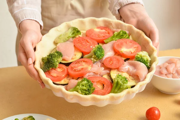 Mutfak masasında sebzeli tavuk turtası tutan bir kadın.