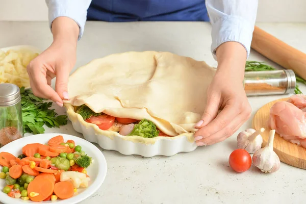 Mutfak masasında sebzeli tavuk güveci hazırlayan kadın.