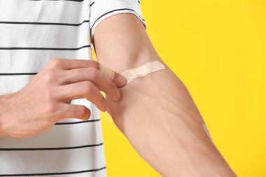 Sarı arka planda koluna sıva uygulayan genç adam, yakın plan.