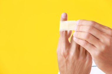 Genç adam sarı arka planda parmağına sıva uyguluyor, yakın plan.