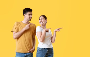 Genç dedikoducu çift sarı arka plandaki bir şeyi işaret ediyor.