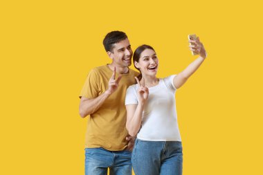 Sarı arka planda selfie çeken genç bir çift.