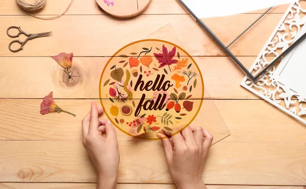 Woman making decoration with dried pressed flowers on wooden background. Hello fall