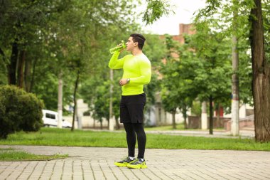 Parkta koştuktan sonra su içen kaslı genç adam.