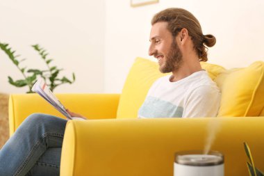 Genç adam modern nemlendiriciyle odada gazete okuyor.