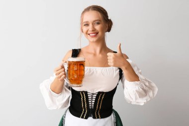 Geleneksel Alman kostümlü güzel bir kadın ve bir kupa birayla gri arka planda baş parmak hareketi gösteriyor.
