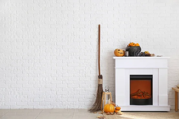 Modern fireplace with Halloween decor near white brick wall