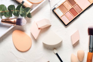 Hafif arkaplanda şık makyaj süngerleri ve dekoratif kozmetik ürünleri