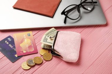 Cüzdanında para ve pembe ahşap arka planda dizüstü bilgisayar var.