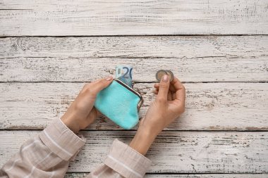 Hafif ahşap arka planda cüzdan ve sikke tutan bir kadın.