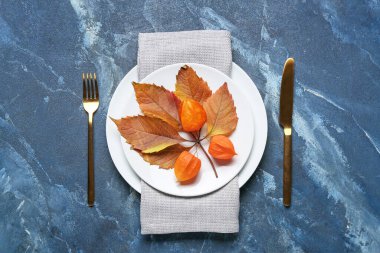 Çatal bıçak, filsalis, sonbahar yaprakları ve renk arkaplanlı peçeteyle Şükran Günü sofrası.