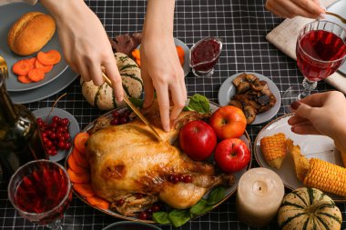 Şükran Günü için servis edilen ziyafet masasında lezzetli kızarmış hindi kesen bir kadın.