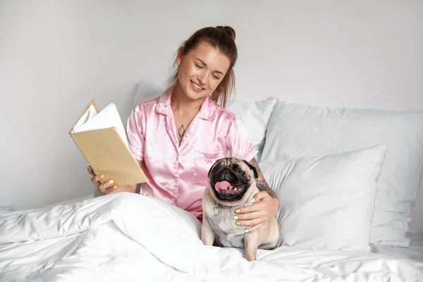 Mujer Joven Con Lindo Perro Pug Libro Lectura Dormitorio — Foto de Stock
