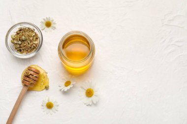 Kavanoz dolusu tatlı bal ve açık arkaplanda kurutulmuş papatya çiçeğiyle kompozisyon