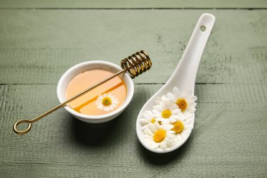 Bir kase tatlı bal ve ahşap arka planda papatya çiçeği.