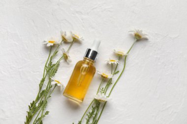 Hafif arkaplanda bir şişe yağ ve papatya çiçeği.