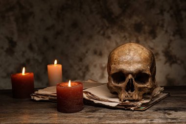 Kitap ve parlak mumlarla dolu bir insan kafatası.
