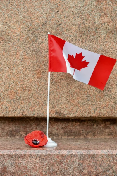 Poppy flower and flag of Canada on stone monument. Remembrance Day