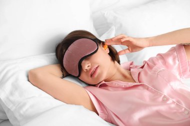 Yatağında kulak tıkacı olan genç bir kadın.