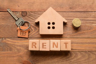 Kelime RENT evden anahtar ve ahşap arka planda madeni paralar