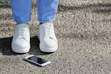 Kadın bacakları ve hasarlı cep telefonu kaldırımda, yakın plan.