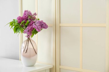 Katlanan ekranın yanındaki masada leylak çiçekli vazo