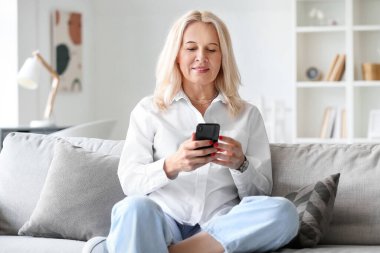 Evde cep telefonu kullanan güzel, olgun bir kadın.