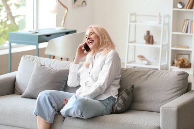 Evde cep telefonuyla konuşan güzel olgun bir kadın.