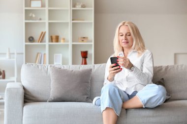 Evde cep telefonu kullanan güzel, olgun bir kadın.