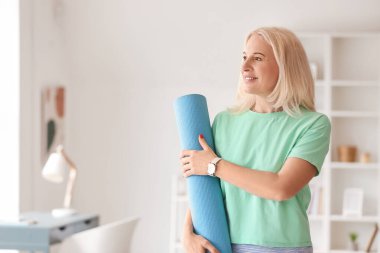 Evde yoga minderli güzel olgun bir kadın.