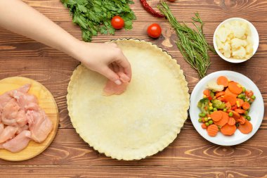 Ahşap arka planda tavuk turtası hazırlayan kadın.