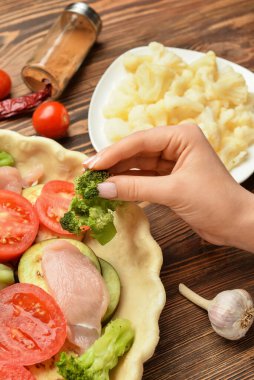 Ahşap arka planda sebzeli tavuk turtası hazırlayan kadın, yakın plan.