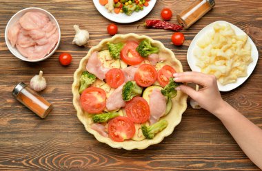 Ahşap arka planda sebzeli tavuk güveci hazırlayan kadın.