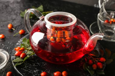 Siyah arka planda bir kap lezzetli gül çayı ve böğürtlen.