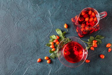 Bir bardak lezzetli gül kalçası çayı, böğürtlen ve siyah arka planda içecek.