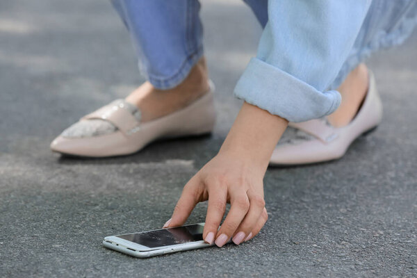 Женщина собирает поврежденный мобильный телефон с тротуара на улице, крупным планом