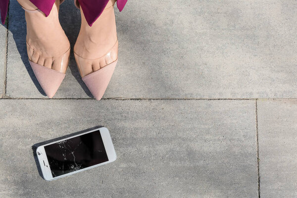 Ноги женщины на каблуках и поврежденный мобильный телефон на улице, крупный план