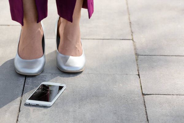 Ноги женщины на каблуках и поврежденный мобильный телефон на улице, крупный план