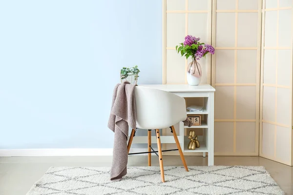 Desk with lilac flowers in vase and folding screen near blue wall