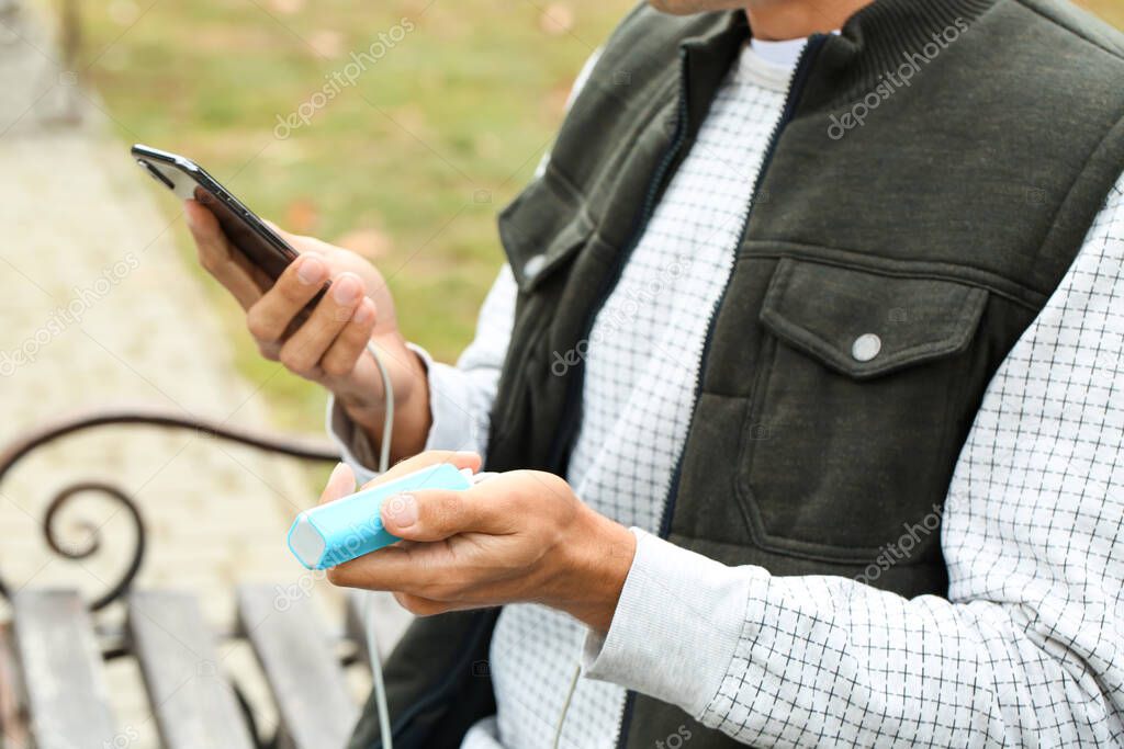 Young man with phone and power bank outdoors, closeup
