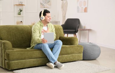 Tabletli mutlu adam evde sesli kitap dinliyor.