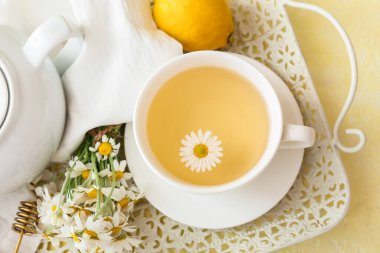 Bir fincan lezzetli papatya çayı, çiçekler ve limonlu tepsi.