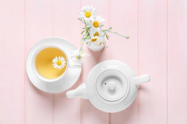 Çaydanlık ve bir fincan lezzetli papatya çayı ve renkli ahşap arka planda çiçekler.