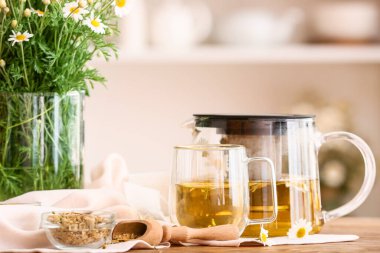 Çaydanlık ve bir fincan lezzetli papatya çayı, masada çiçekler.