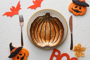 Beyaz arka planda balkabağı şekilli tabak, çatal bıçak takımı ve Cadılar Bayramı dekoru.