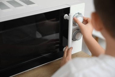 Küçük çocuk mikrodalga fırında yemek ısıtıyor.