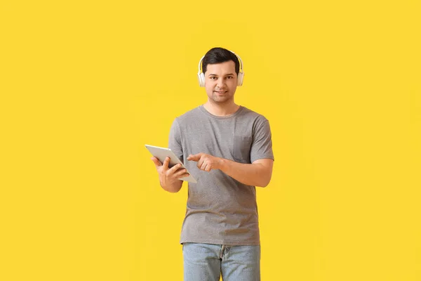 タブレットコンピュータとヘッドフォンを持つ若い男の色の背景 — ストック写真