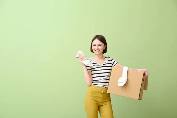 Young woman with wardrobe box and shoes on color background